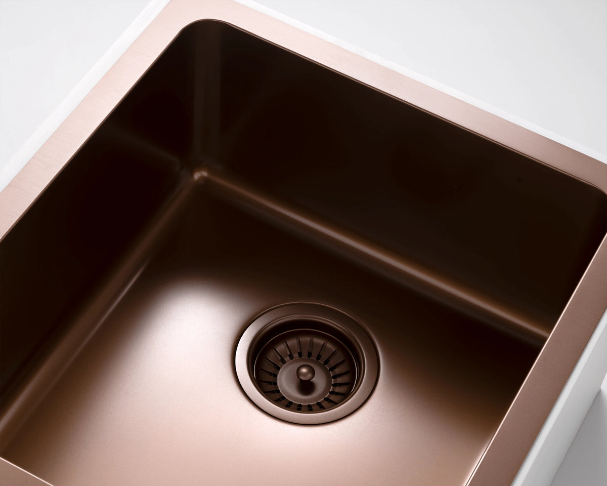 A close-up of a titan single bowl kitchen sink with an aged brass PVD finish and a matching drain, shown against a white background.